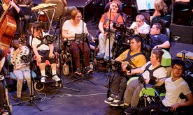 Young musicians in wheelchairs performing on stage with iPads.