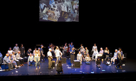 A group of performers on stage with a screen behind showing a film