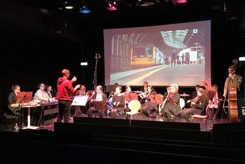 A group of musicians performing in front of a screen showing a film.