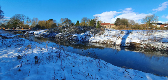 A photograph of a river, with snow covered banks and patches of shadow and sunlight