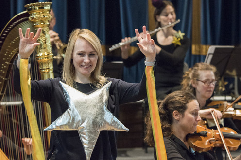 A woman using British Sign Language to interpret a performance by an orchestra.