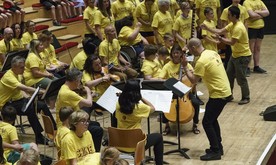 A mid-short of a large group of musicians on stage, all in yellow t-shirts.