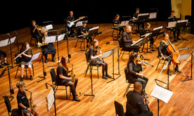 A group of young and older musicians sat socially distanced on a stage